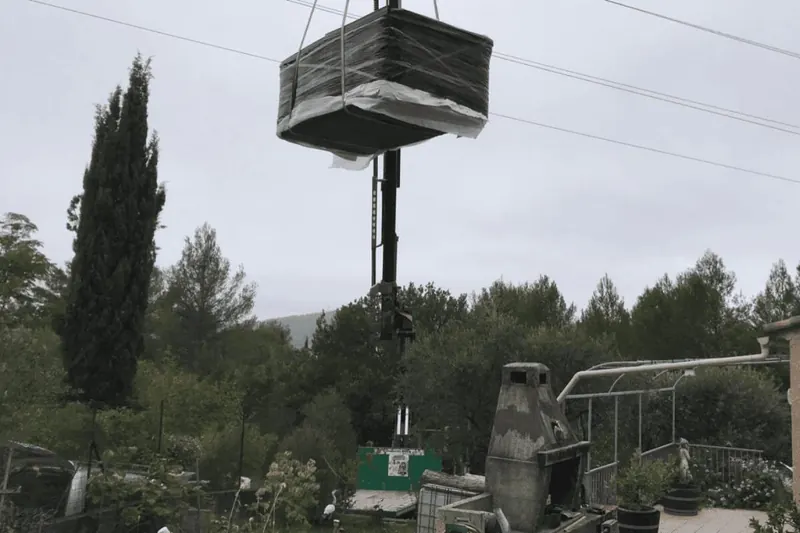 Spa emballé suspendu au crochet d'une grue au-dessus des arbres du jardin, à Alès