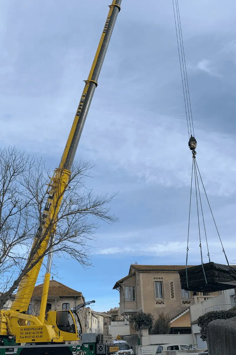 Grue mobile jaune dépliée dans une rue de Saint-Jean-de-Védas, le spa suspendu au-dessus des toits