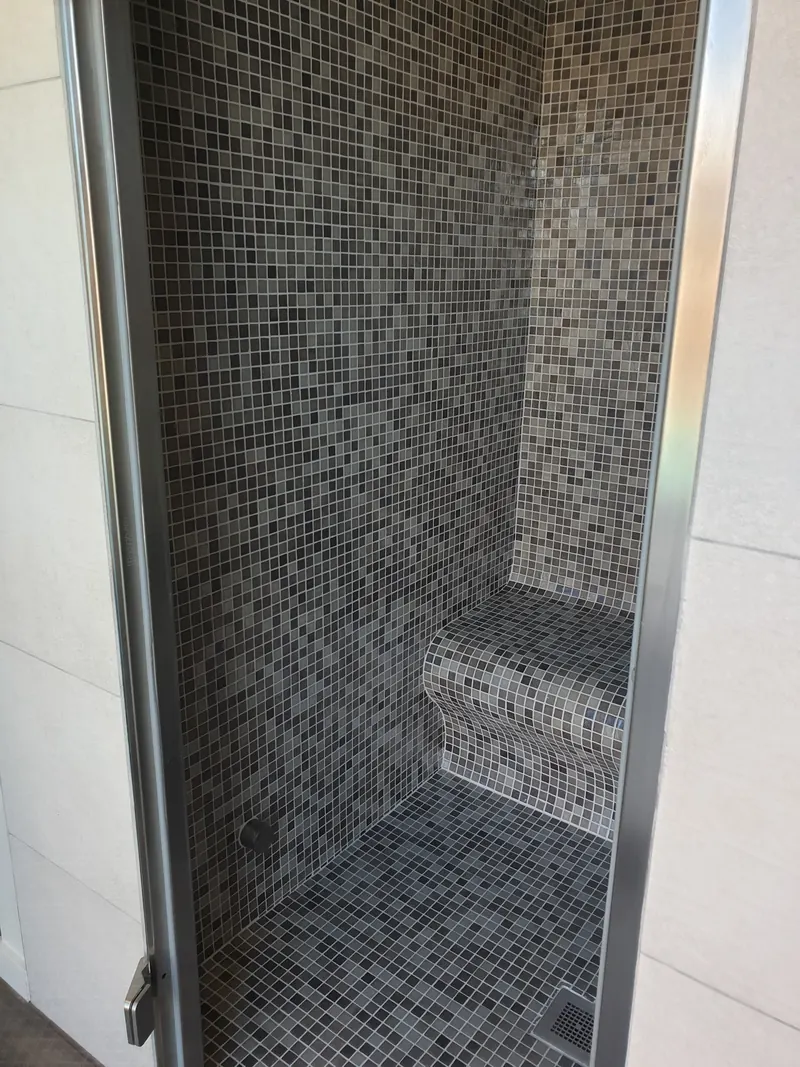 Intérieur d'un hammam en mosaïque grise avec banquette galbée, vu par la porte ouverte, à Perpignan