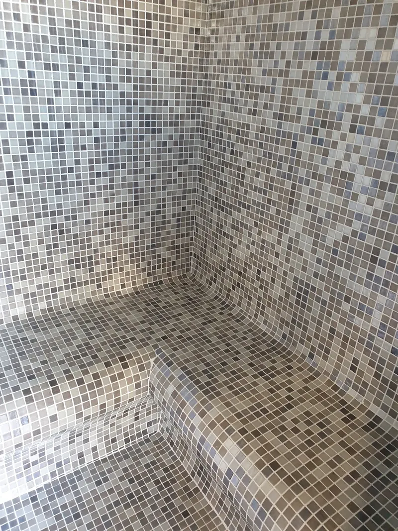Banquette galbée en mosaïque grise dans l'angle d'un hammam à Perpignan