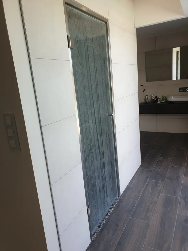 Porte vitrée de hammam prise dans le mur carrelé clair d'une salle de bains à Perpignan