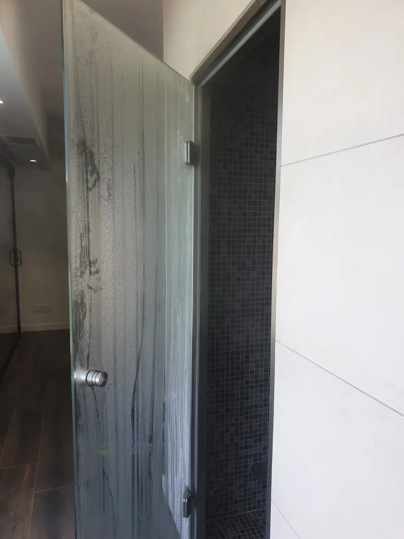 Porte vitrée ouverte sur l'intérieur d'un hammam habillé de mosaïque grise à Perpignan