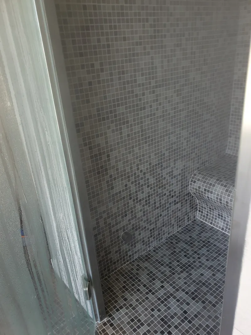 Intérieur d'un hammam en mosaïque grise, avec un banc carrelé aux bords arrondis, à Perpignan