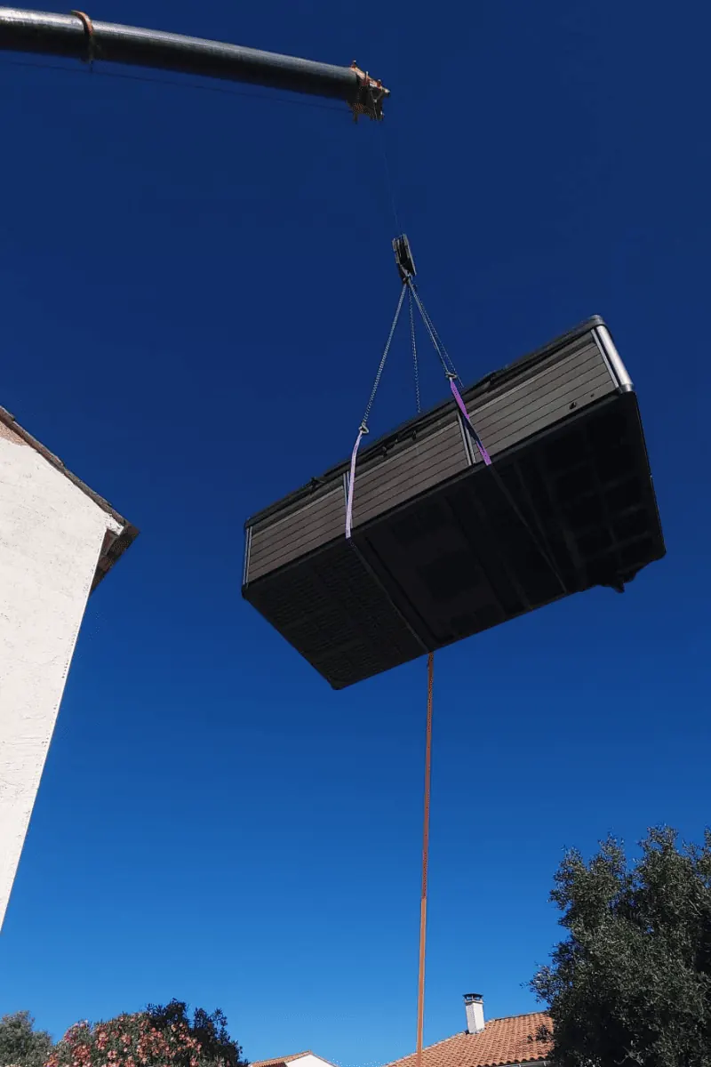 Spa de nage suspendu à la grue sous un ciel bleu, au-dessus de la maison