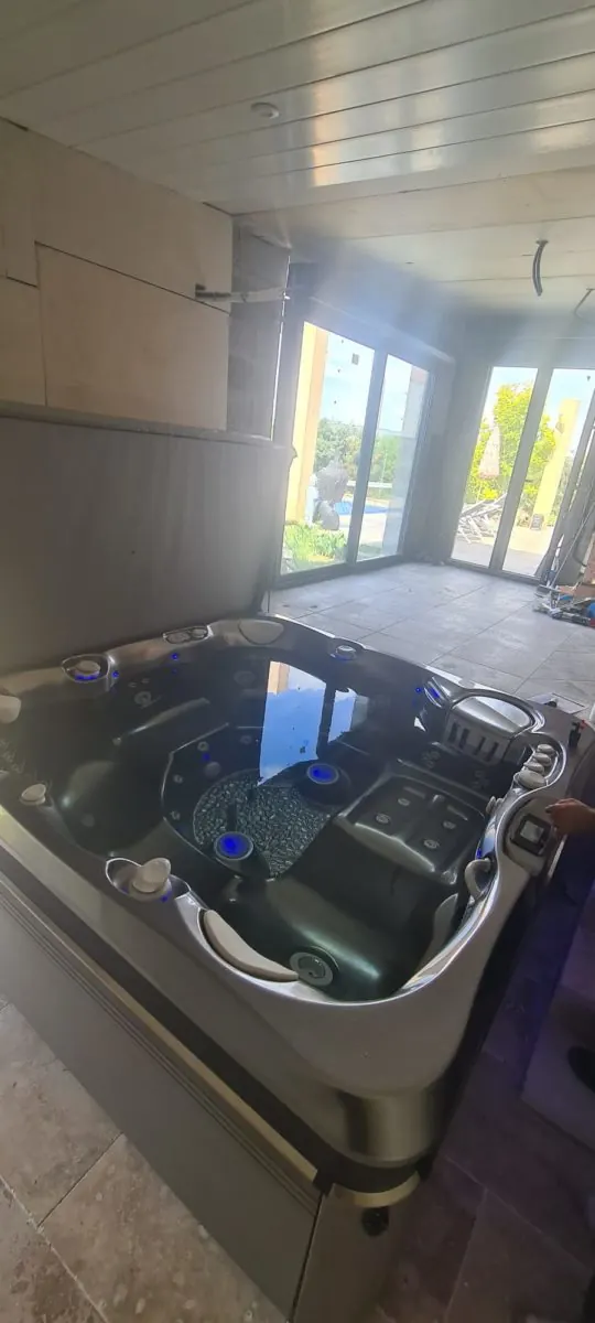 Grand spa Caldera Tahitian installé dans une pièce de bien-être carrelée à Gigean, baies vitrées au fond