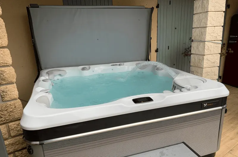 Spa Caldera Tahitian rempli, couvercle relevé, sous une terrasse couverte de Bagnols-sur-Cèze