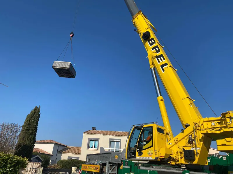 Grue jaune BREL soulevant le spa au-dessus des maisons voisines, à Nîmes