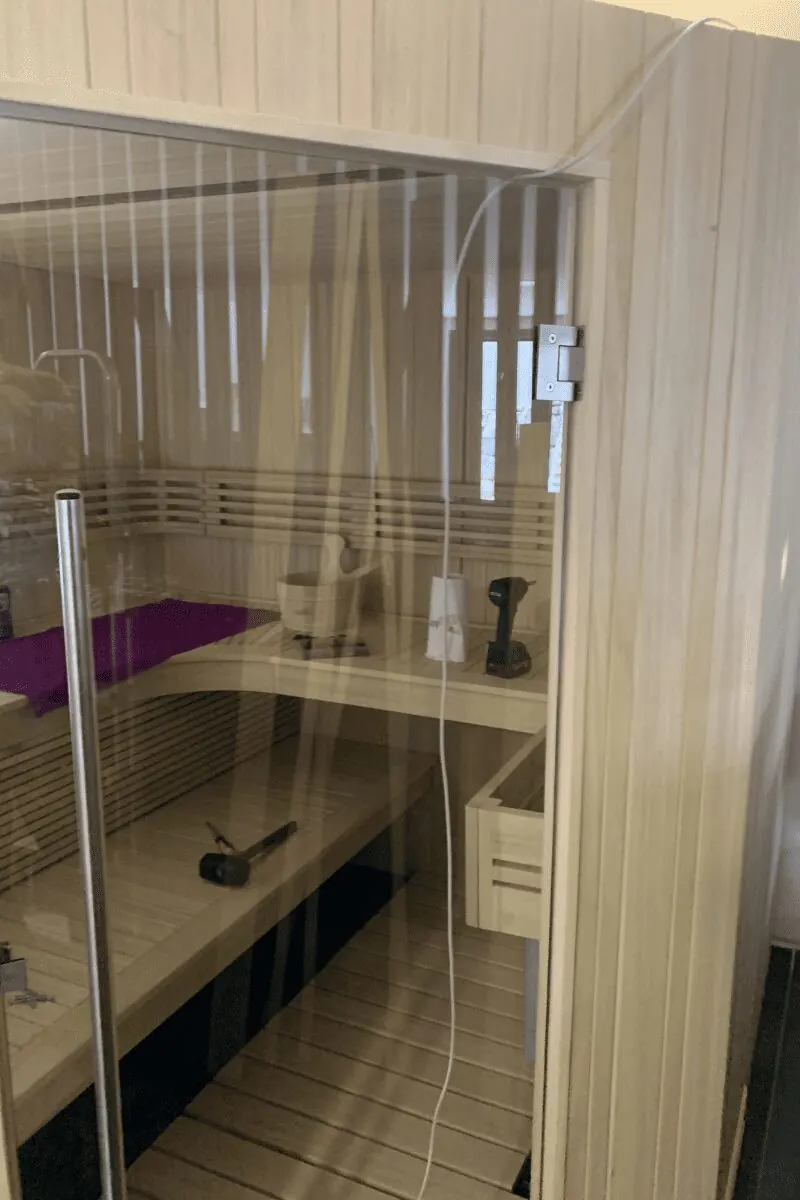 Montage de la porte vitrée d'un sauna finlandais d'angle, à Thézan-lès-Béziers