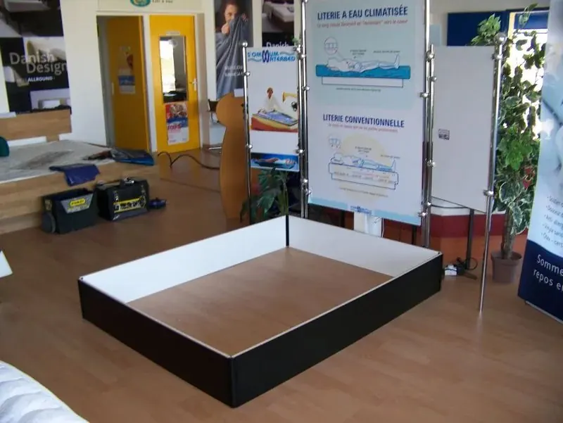 Socle de lit à eau assemblé au showroom de Sommum Wellness, affiches de literie au fond