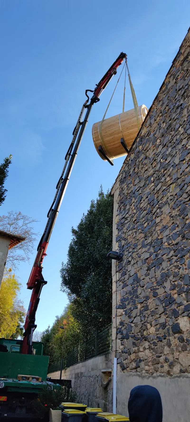 Flèche de la grue déployée, sauna tonneau suspendu le long d'un haut mur de pierre