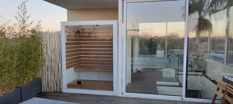 Vue générale du sauna vitré et de ses bancs en bois sur la terrasse, face au paysage