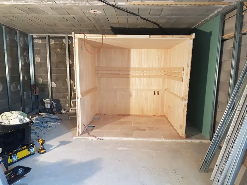 Cabine de sauna en bois clair montée sans sa façade, dans une pièce en travaux à Mèze