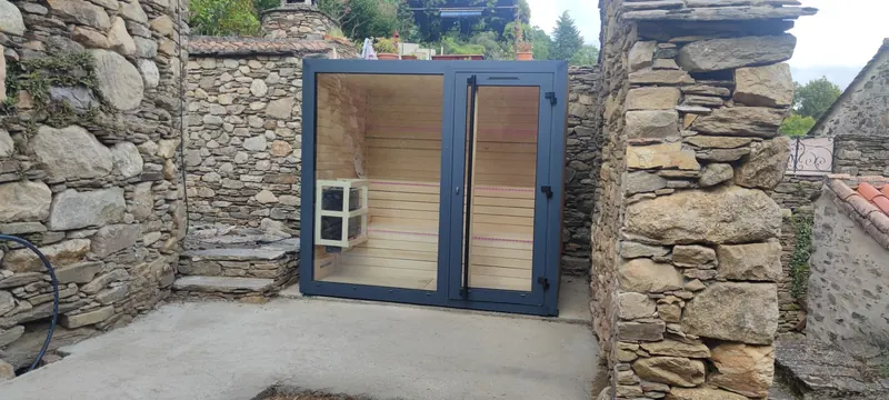 Sauna vu de l'extérieur en perspective, encadré de murs de pierre en ruine
