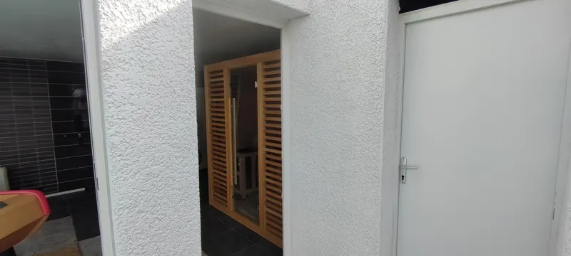 Sauna en bois vu de face, dans une salle claire aux finitions blanches, baies vitrées proches