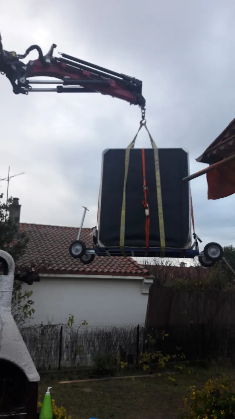 Spa sanglé sur son chariot, suspendu à la grue au-dessus d'un jardin et d'un toit de tuiles