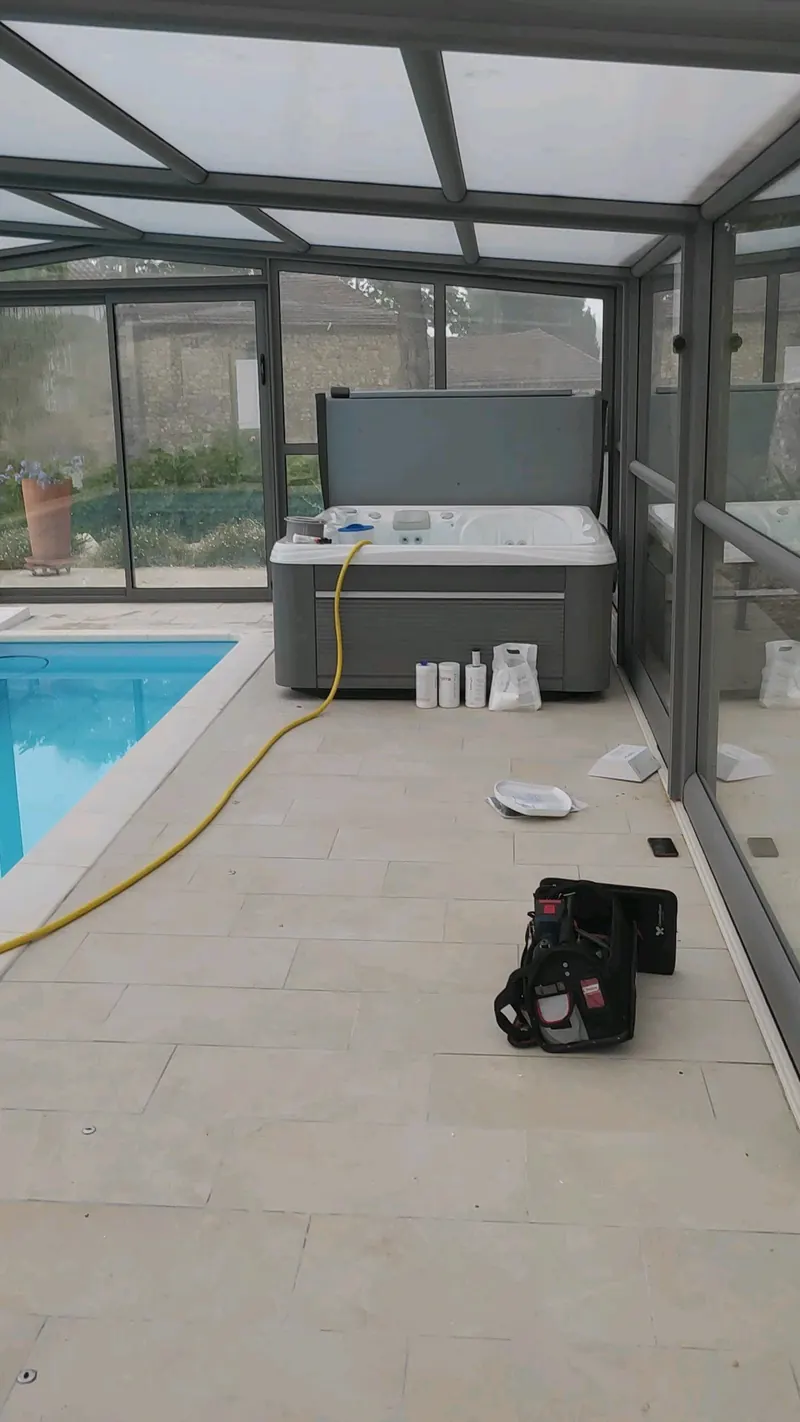Spa gris sous l'abri vitré, piscine à gauche, sac à outils et flacons au sol