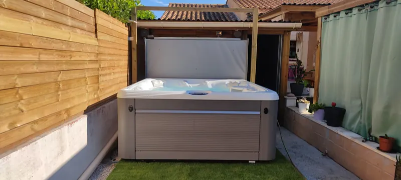 Vue d'ensemble du spa blanc sous la pergola en bois, patio fermé par une clôture