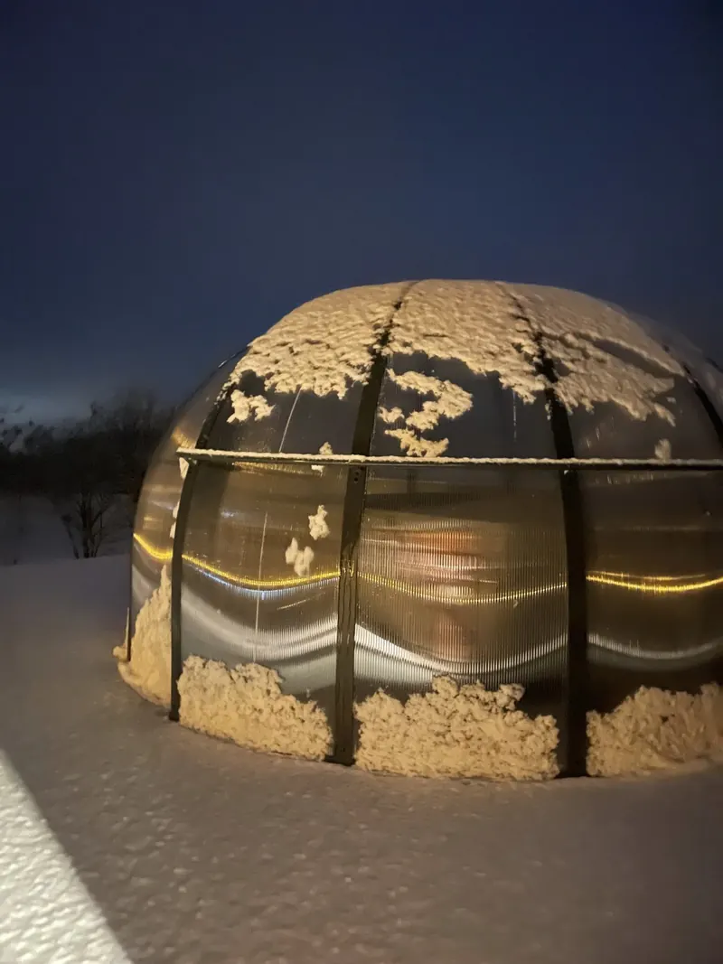 Dôme transparent éclairé de l'intérieur, de nuit, entouré de neige