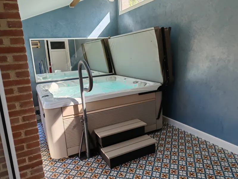 Spa beige et blanc, couverture relevée, pièce aux murs bleus, carrelage à motifs et miroir mural