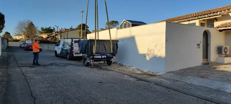 Spa sous bâche sur une remorque, sangles tendues vers la grue, mur blanc et fourgon