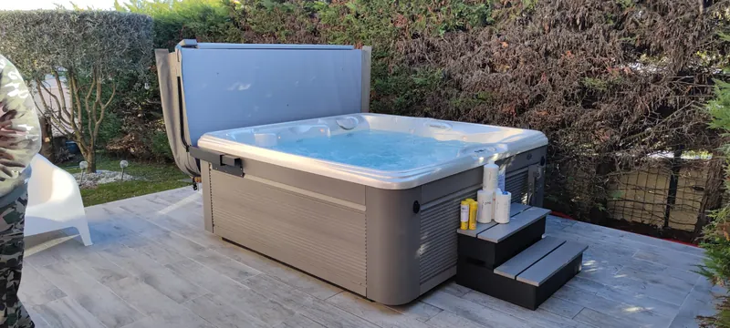 Spa en place sur la terrasse carrelée, couvercle relevé, marches et flacons d'entretien