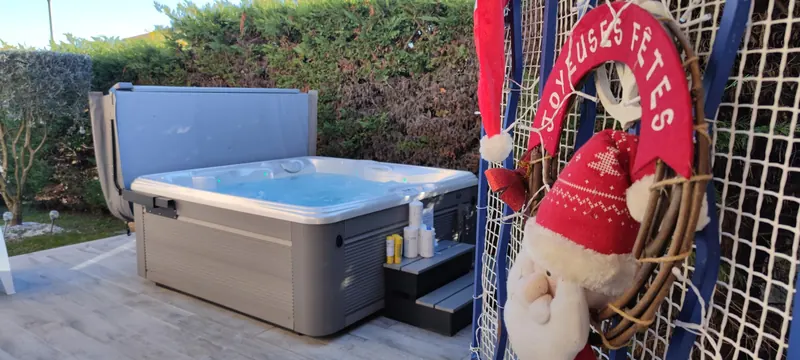 Spa rempli d'eau, décoration « Joyeuses fêtes » et Père Noël en peluche au premier plan