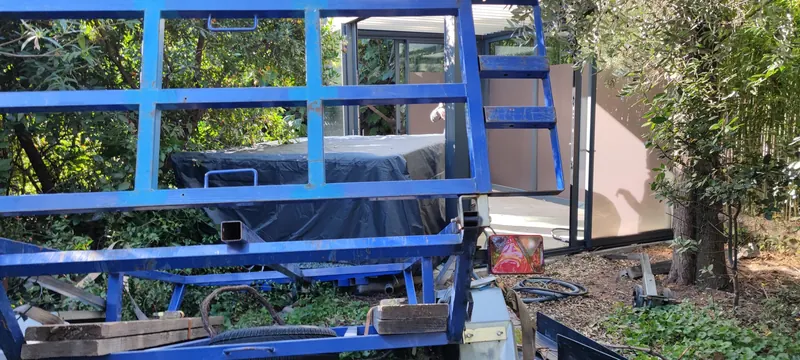 Remorque bleue au premier plan, spa bâché et structure vitrée au fond