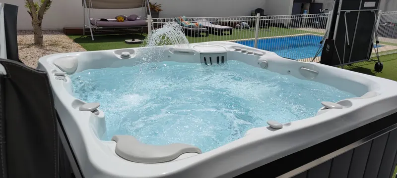 Spa en eau avec une fontaine, piscine et barrière blanche derrière