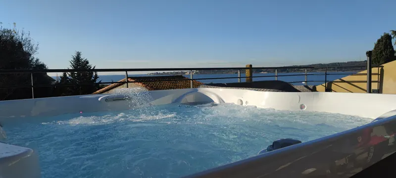 Spa à coque blanche, jets actifs, plan d'eau et garde-corps métallique en arrière-plan