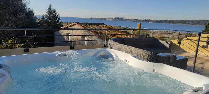 Spa en fonctionnement, salon tressé sur la terrasse et plan d'eau au loin