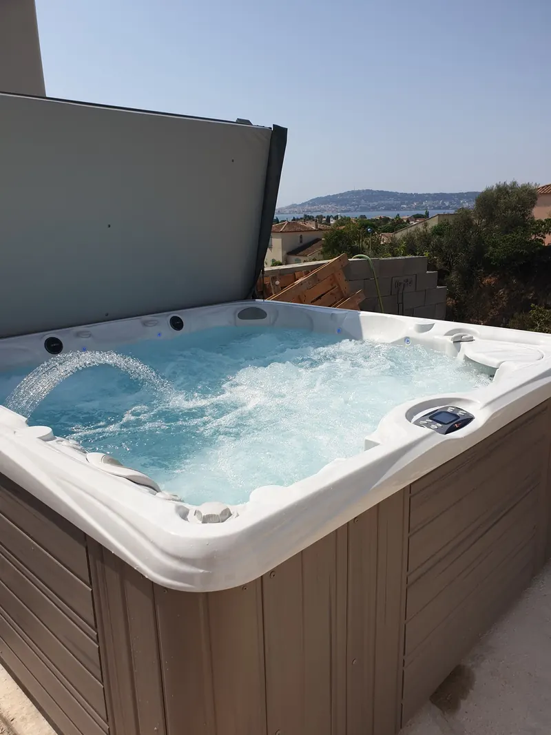 Spa rempli, jets et cascade en marche, couvercle relevé, vue sur les toits et l'eau à Balaruc-les-Bains