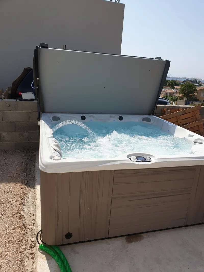 Spa à habillage taupe posé sur une dalle béton au pied d'un muret en parpaings à Balaruc-les-Bains