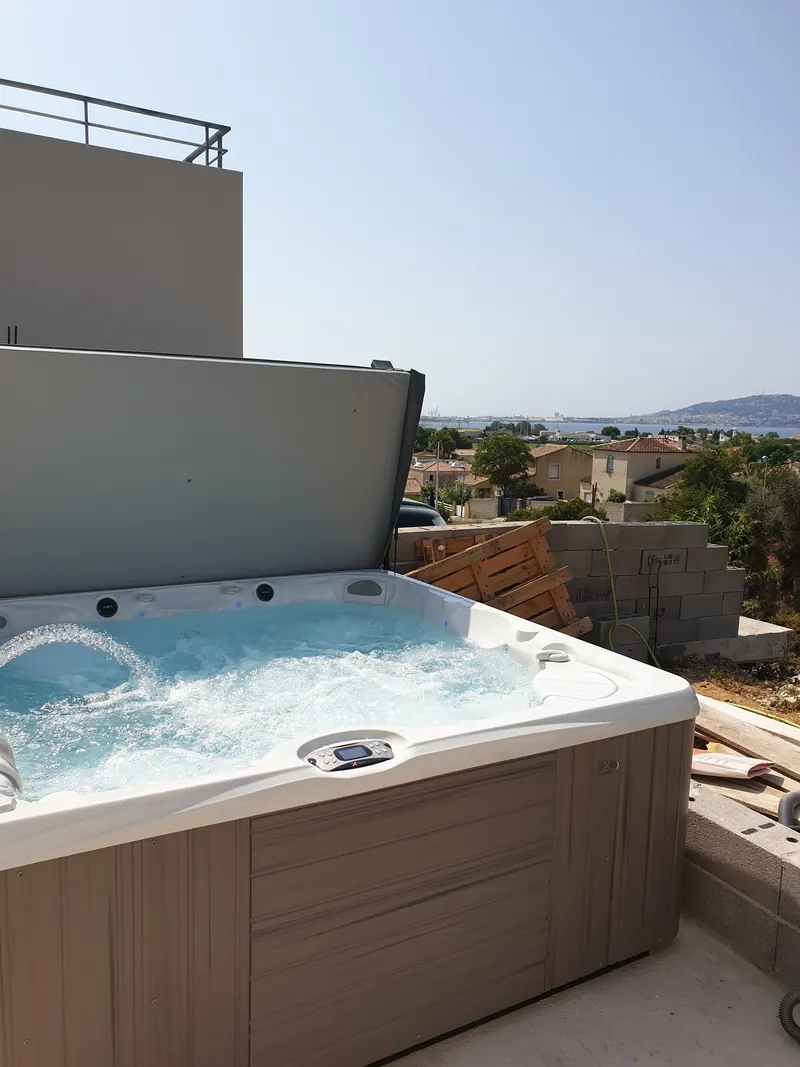 Spa en marche, couvercle relevé, sur une terrasse en béton avec vue sur l'eau à Balaruc-les-Bains