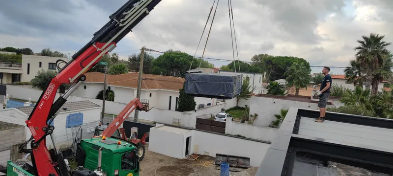 Caisson du spa levé très haut par la grue rouge, sur fond de ciel bleu