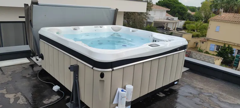 Spa blanc et noir posé sur la terrasse, eau turquoise, maisons en arrière-plan