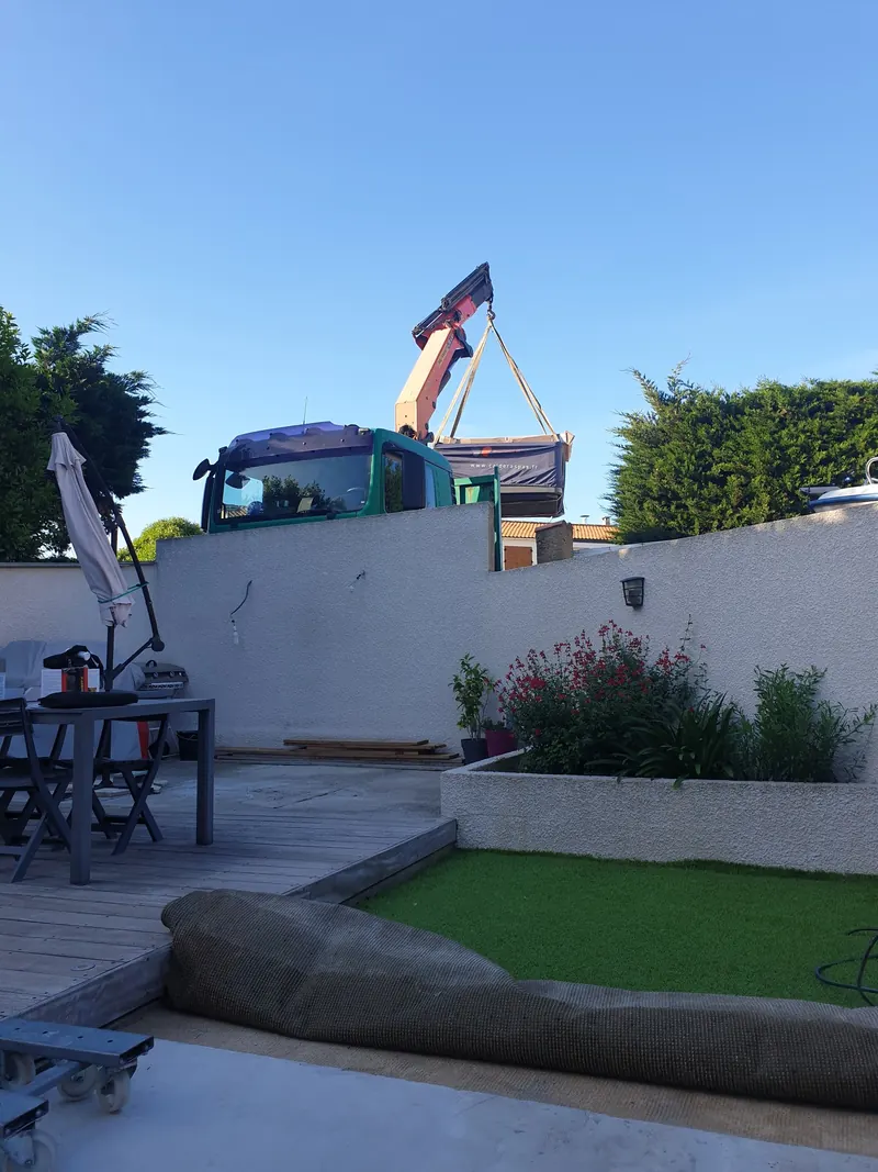 Spa emballé soulevé par la grue, au-dessus du muret de clôture