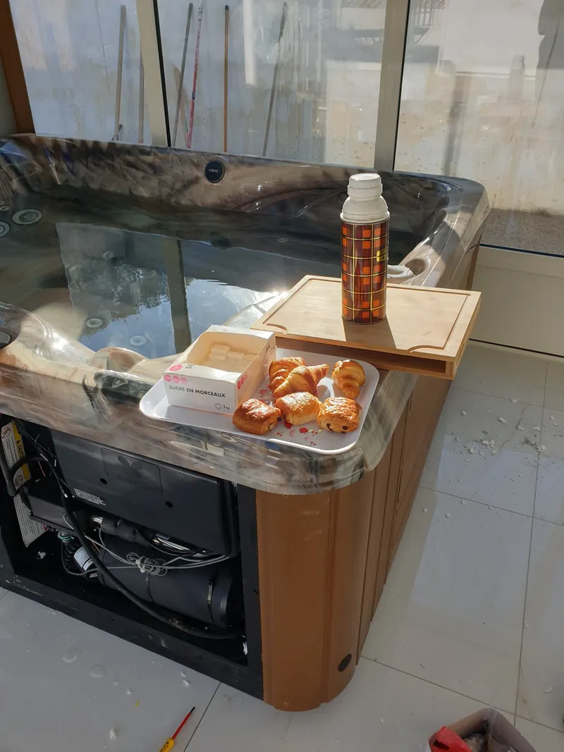 Spa à l'habillage bois, panneau retiré sur le compartiment technique, plateau de viennoiseries sur le rebord