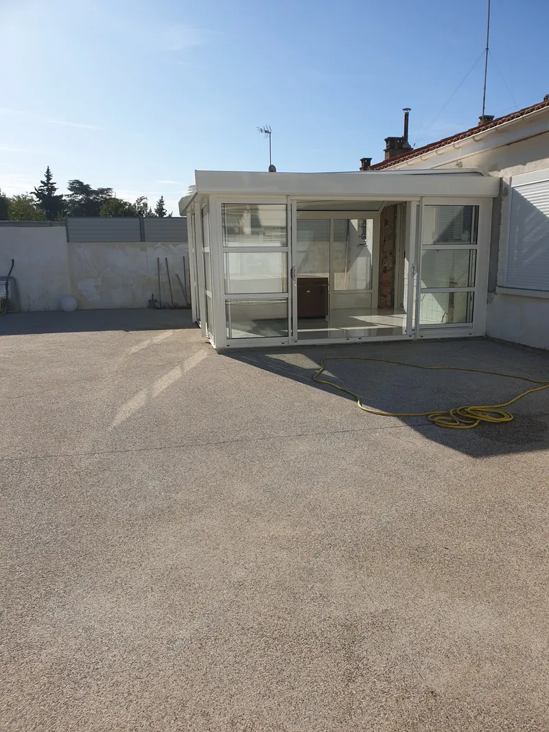 Véranda vitrée accolée à une maison de Béziers, spa visible à l'intérieur depuis la cour