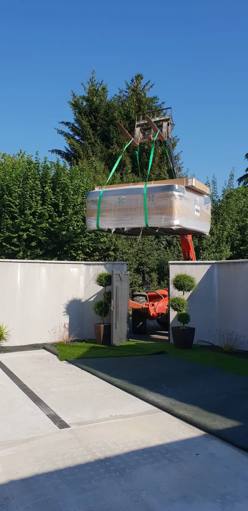 Spa Caldera emballé, suspendu au chariot télescopique au-dessus du mur d'une cour à Billiat