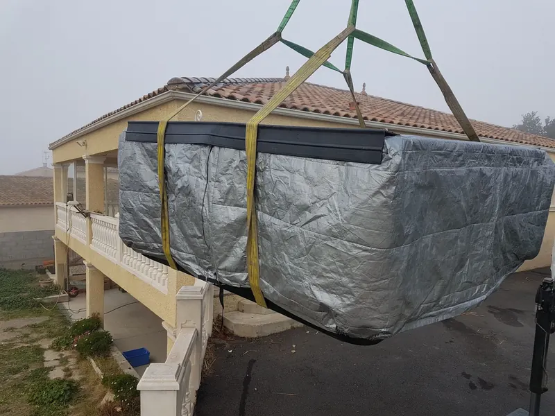 Spa bâché suspendu à la grue devant le balcon à balustres d'une maison à Lespignan