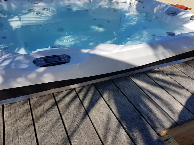 Rebord du spa et son panneau de commande, posé sur une terrasse en lames de bois grises