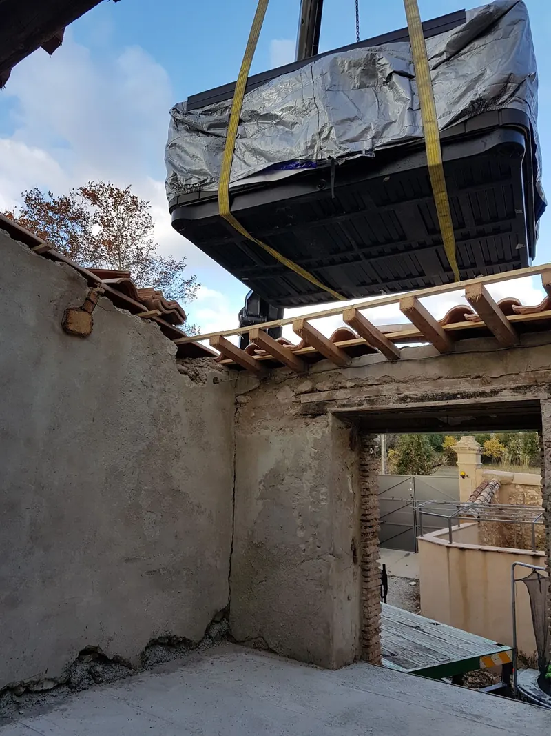 Spa hissé à la grue au-dessus d'un mur de pierre, avant sa descente sur la dalle béton à Montpeyroux