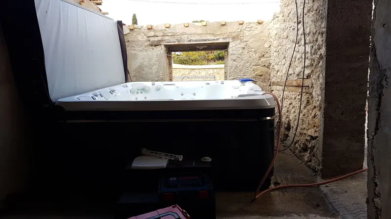 Spa à cuve claire, couvercle relevé, posé entre de vieux murs de pierre à Montpeyroux