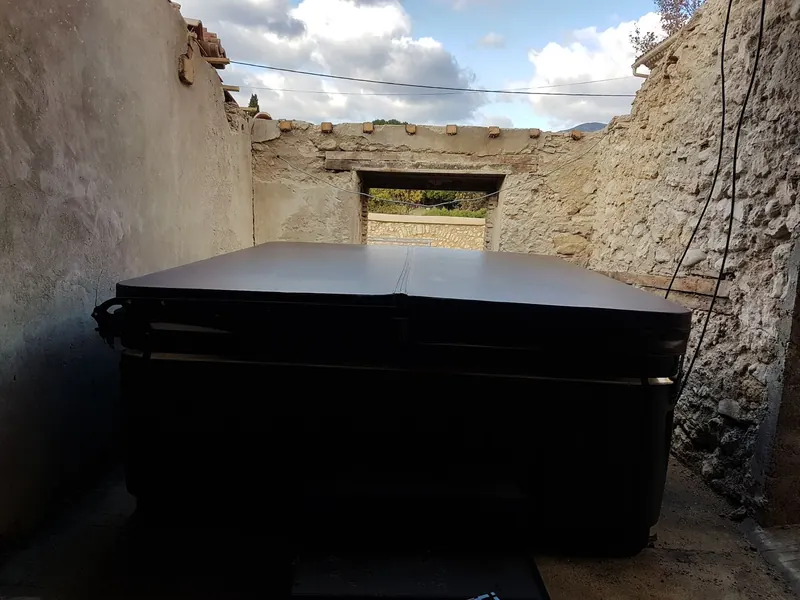 Spa fermé par sa couverture sombre, installé entre des murs de pierre ouverts sur le ciel à Montpeyroux