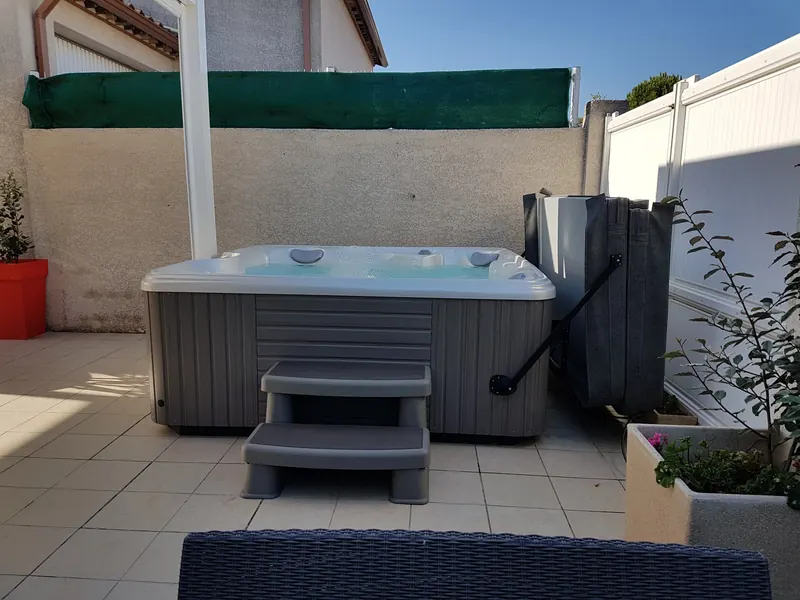 Spa à jupe grise avec escalier et lève-couverture au fond d'une terrasse carrelée à Lavérune