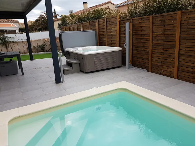 Piscine au premier plan et spa installé dans l'angle de la terrasse, près d'une pergola, à Mèze