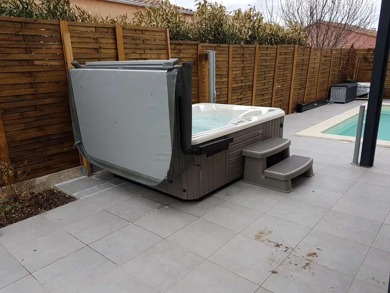 Spa vu de côté avec couvercle replié sur le lève-couvercle et marchepied, piscine au fond, à Mèze