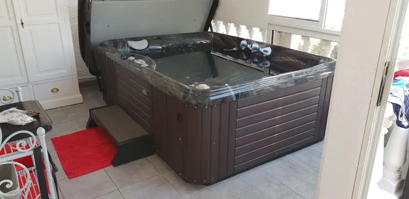 Spa Caldera Celio à coque marbrée noire posé sur carrelage dans une pièce vitrée à Sète, marchepied devant