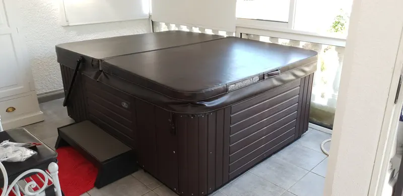 Spa Caldera Celio fermé par sa couverture brune, marchepied posé devant, dans une pièce vitrée à Sète