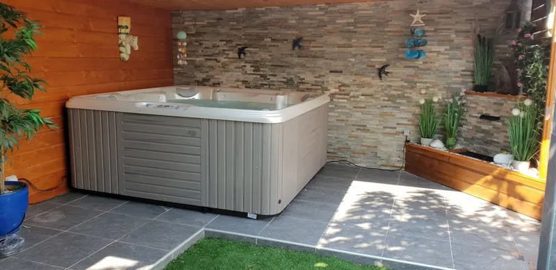 Spa Caldera Marino gris rempli d'eau sous un abri en bois, contre un mur en parement de pierre à Vic-la-Gardiole